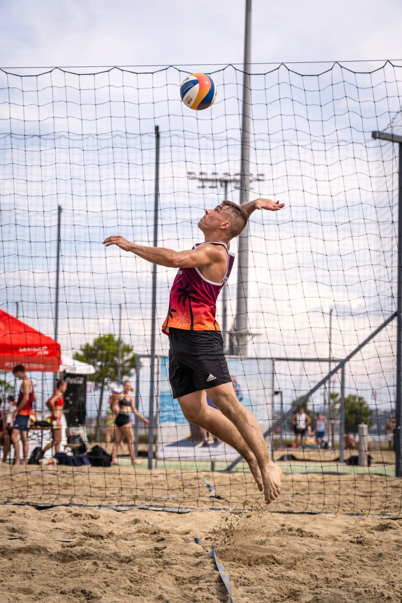 Igralec v Capris Volley dresu med skokom za servis na turnirju odbojke na mivki